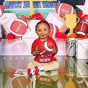 Christian joined the competition — help win amazing prizes! toddler, child, football, sports, toy, red_shirt, beige_pants, socks, smile, indoor, props, trophy, water_bottle, background, stadium, field, decorations, playful, reflection, photography