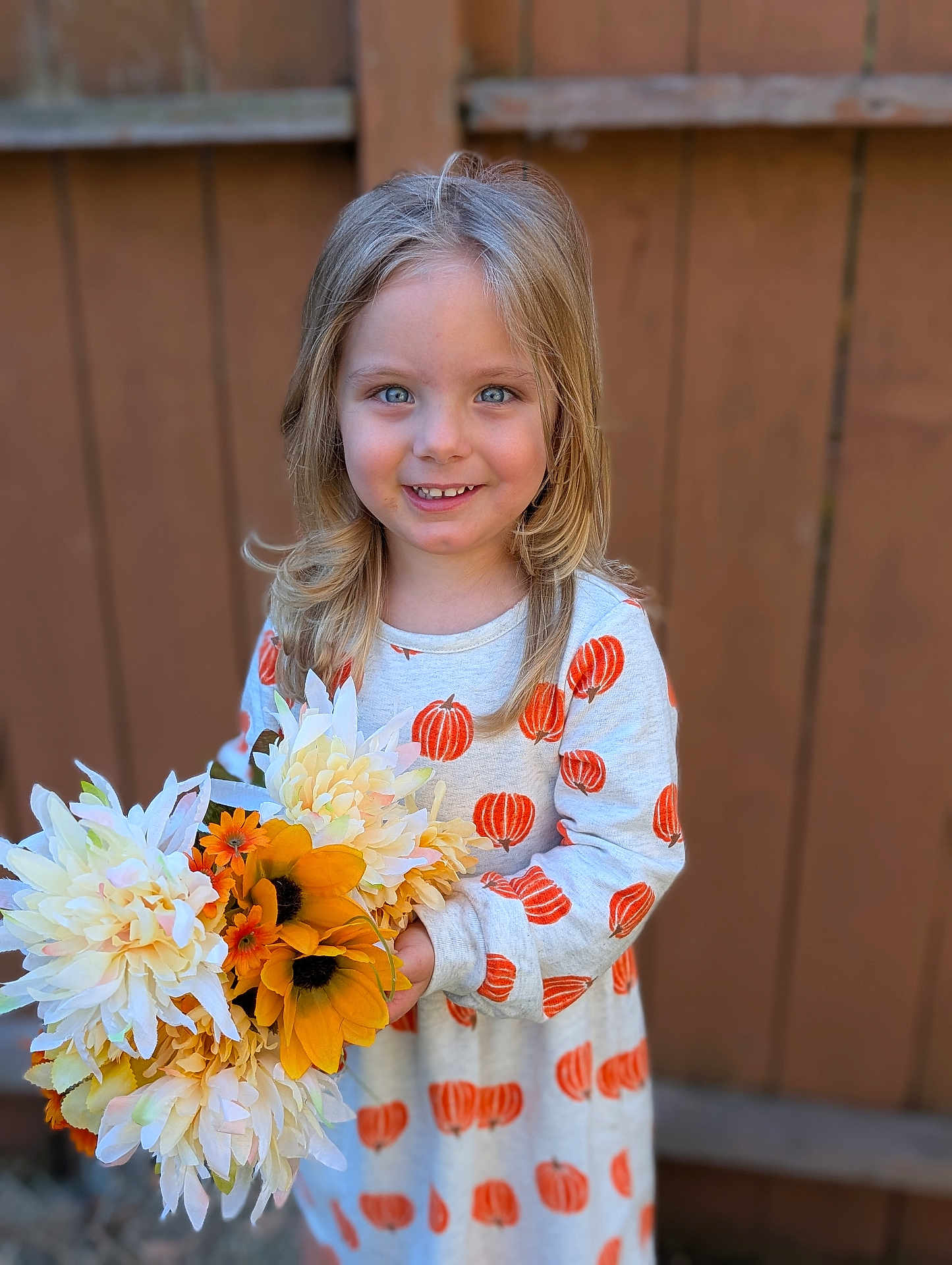 Hope is registered to the contest to win money with this photo: child, girl, smiling, blonde_hair, blue_eyes, flowers, bouquet, pumpkin_pattern, dress, outdoor, wooden_fence, fall, autumn, happy, portrait, person, nature, seasonal, cute, holiday