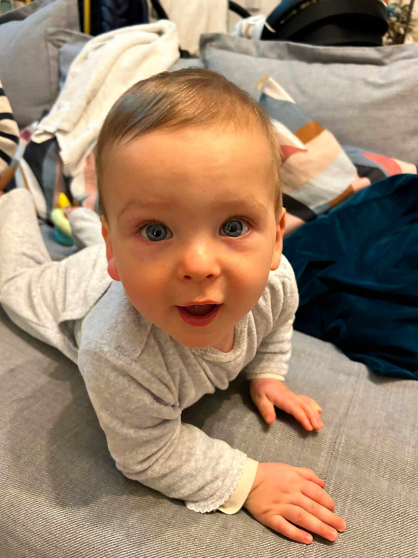 Albin participe au concours pour gagner de l'argent avec cette photo : baby, child, crawling, blue_eyes, gray_couch, blanket, cushion, soft_toys, indoors, clothing, long_sleeve, person, face, hands, curious, expression, home, comfort, cute, closeup