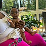 baby, child, person, lap, diaper, drool, hair_buns, pink_pants, hand, plant, porch, outdoor, sunlight, pacifier, toy, furniture, greenery, skin, expression, clothing