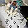 T Ruzin is registered to the contest to win money with this photo: baby, infant, smiling, sitting, cushioned_seat, bed, blanket, pillow, milestone_blanket, numbers, months, clothing, socks, indoor, cozy, happy, raised_hand, face, person, child