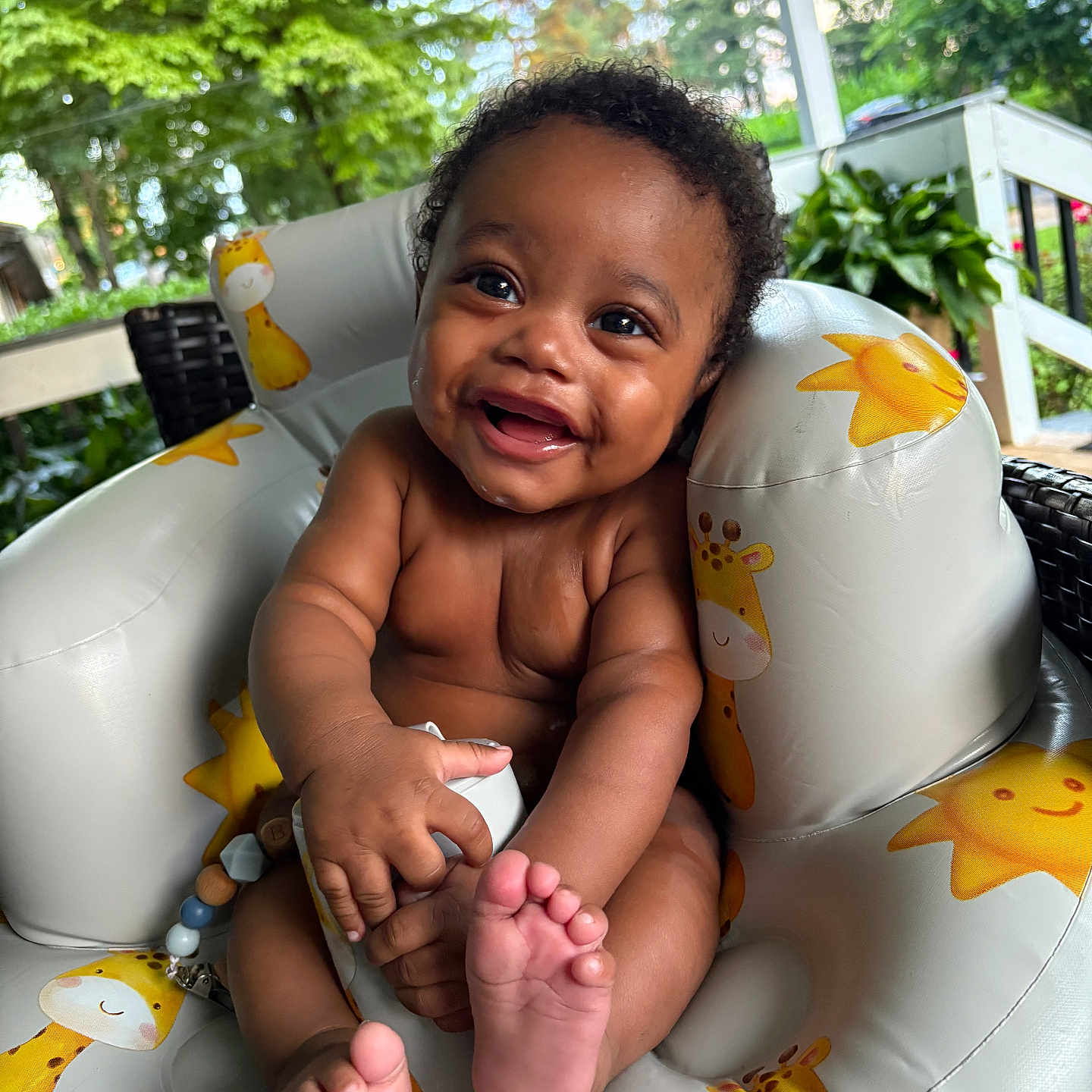 T Ruzin is registered to the contest to win money with this photo: baby, child, comfort, curly_hair, cute, daylight, feet, giraffe_pattern, greenery, hands, happy, infant, inflatable_chair, outdoor, plants, porch, skin, smile, sun_pattern, toy