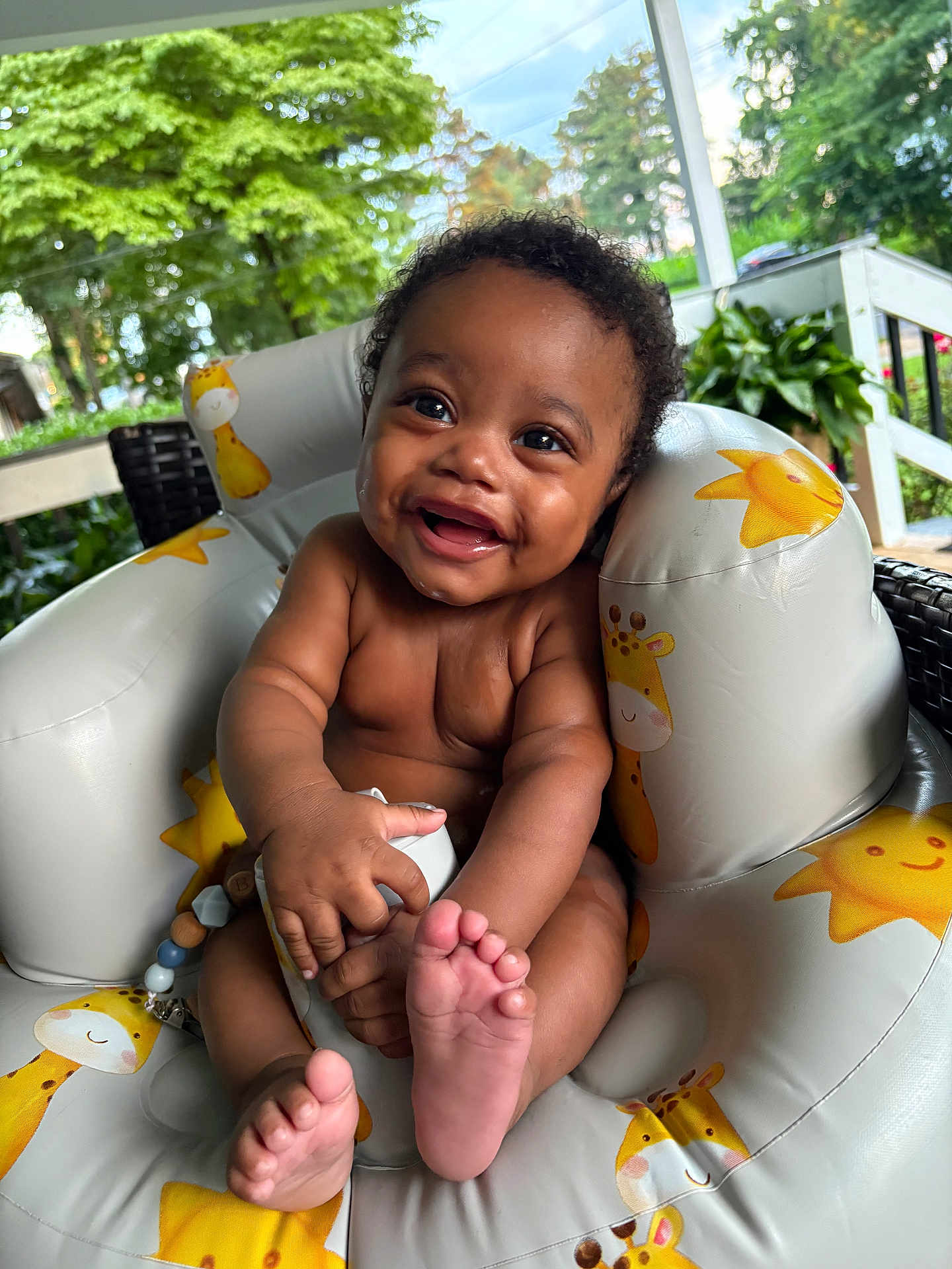 T Ruzin is registered to the contest to win money with this photo: baby, child, comfort, curly_hair, cute, daylight, feet, giraffe_pattern, greenery, hands, happy, infant, inflatable_chair, outdoor, plants, porch, skin, smile, sun_pattern, toy
