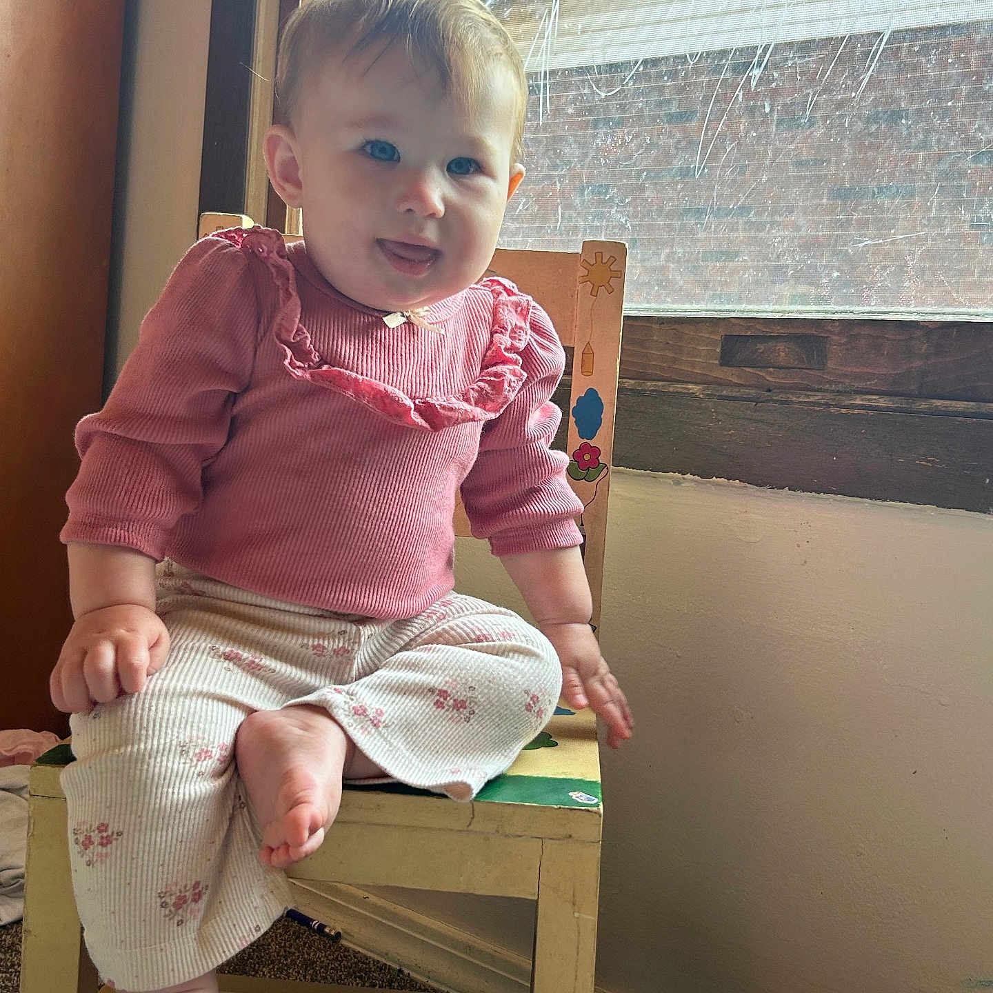 Elisheva is registered to the contest to win money with this photo: baby, blue_eyes, carpet, casual, child, cute, floral_pants, home, indoor, natural_light, person, pink_clothing, playful_expression, sitting, smiling, tongue_out, wall, window, wooden_chair, young_child