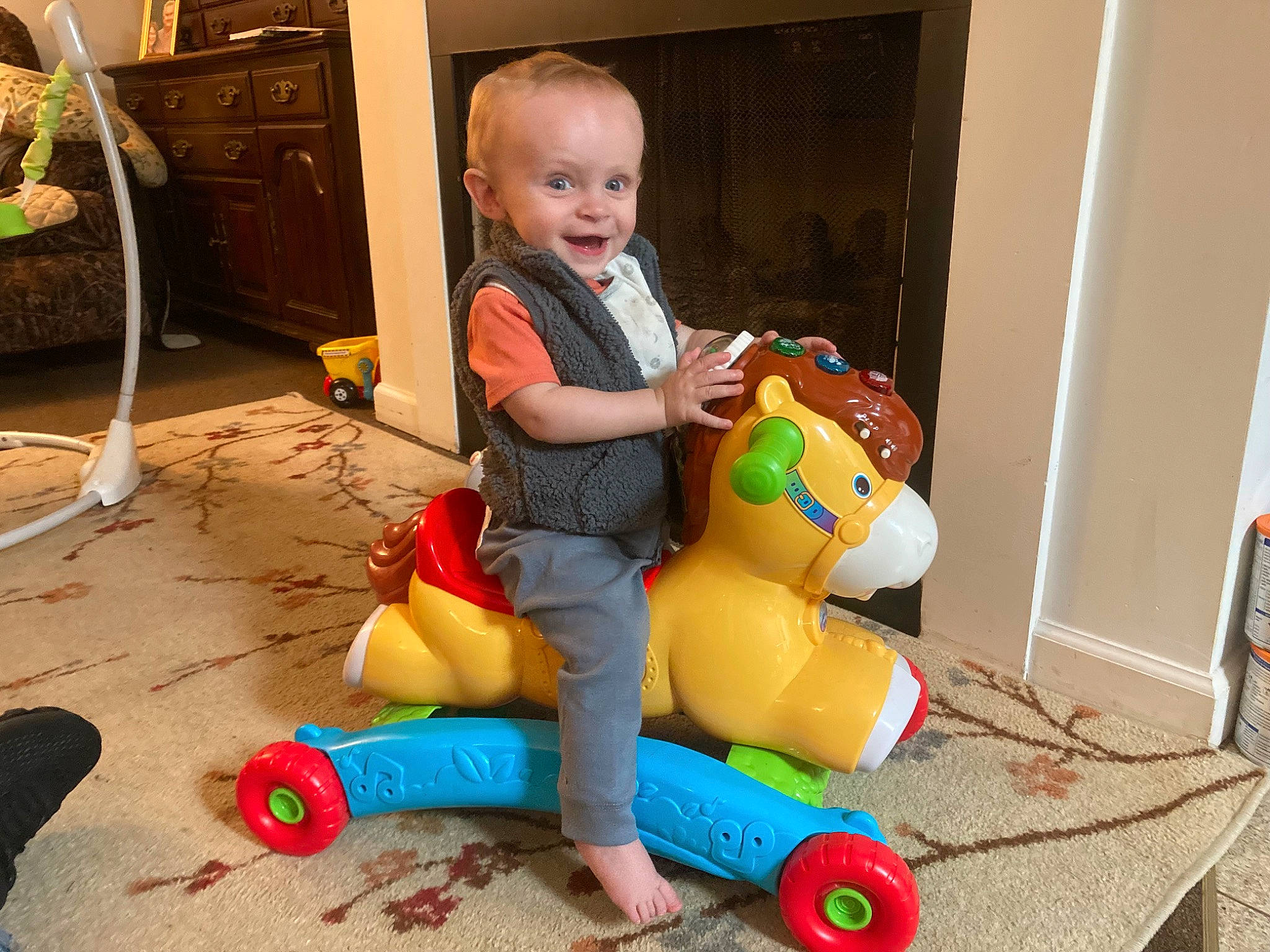 Jaiden is registered to the contest to win money with this photo: baby, baby_toddler_clothing, child, cleanliness, comfort, flooring, fun, human_leg, knee, person, plastic, play, refrigerator, riding_toy, room, sitting, snapshot, toddler, toy, toy_vehicle