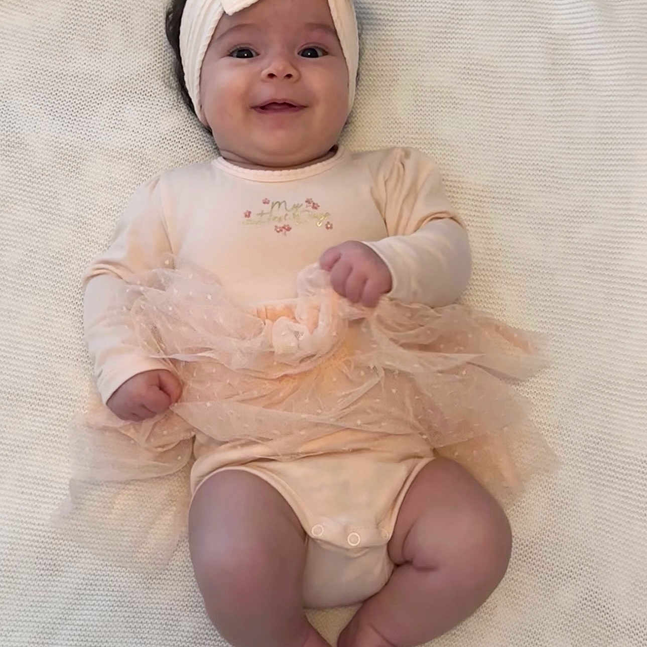 Amélia a rejoint le concours — aidez-le/la à gagner de superbes lots ! adorable, baby, baby_girl, blanket, child, chubby_legs, close_up, cozy, cute, happy, headband, indoors, infant, infant_clothing, lying_down, peach_outfit, portrait, smiling, soft_texture, tutu