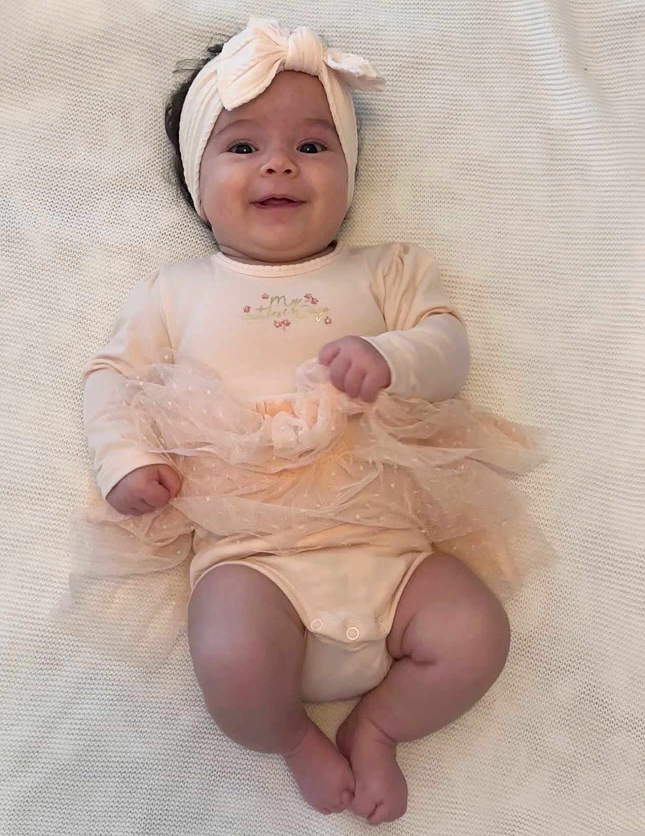 Amélia a rejoint le concours — aidez-le/la à gagner de superbes lots ! baby, infant, smiling, headband, tutu, peach_outfit, lying_down, blanket, cute, happy, chubby_legs, soft_texture, portrait, child, adorable, infant_clothing, baby_girl, close_up, indoors, cozy