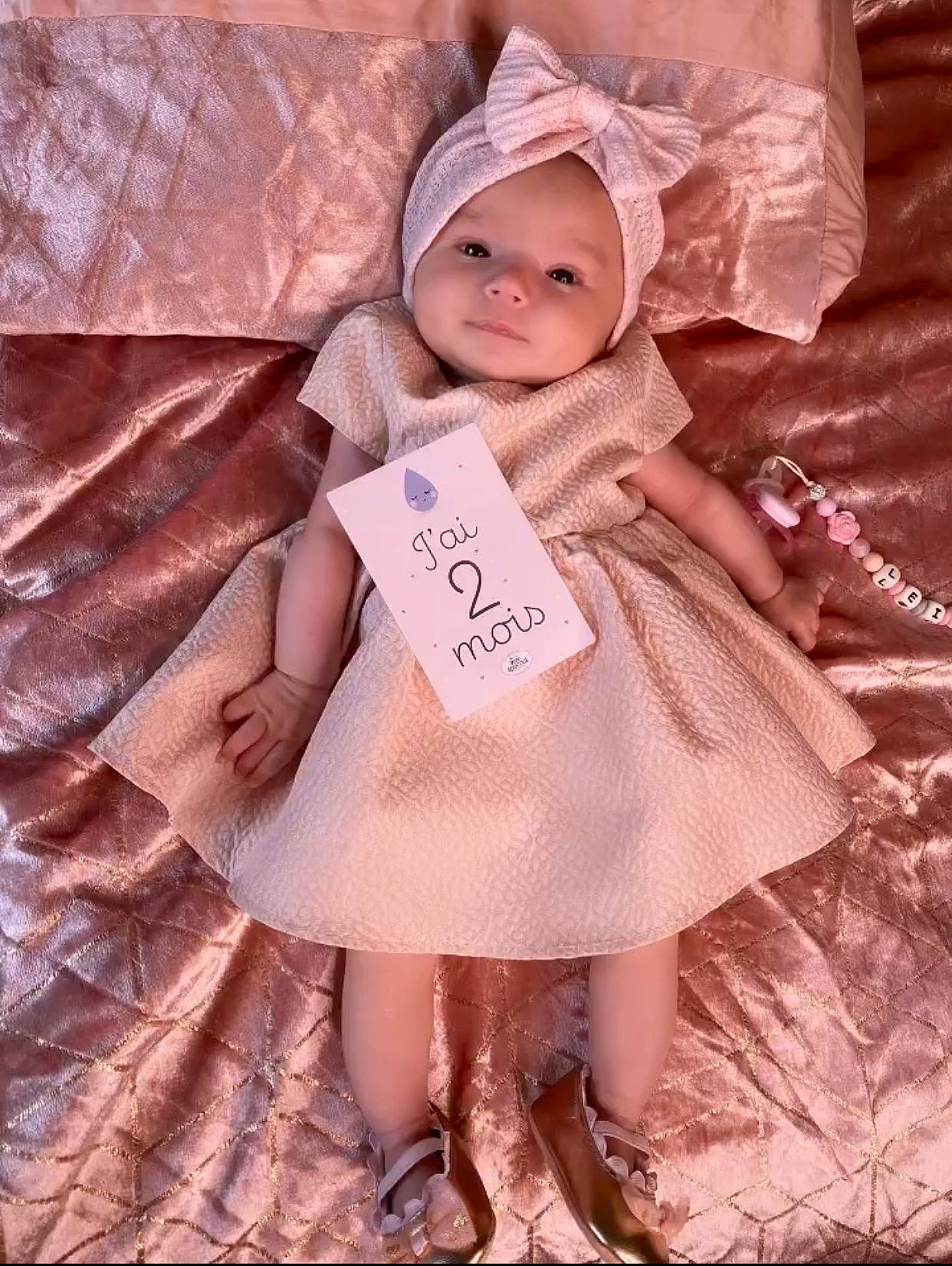 Leïla a rejoint le concours — aidez-le/la à gagner de superbes lots ! baby, baby_toddler_clothing, child, day_dress, dress, fashion_accessory, fashion_design, happy, hat, headwear, human_leg, pattern, peach, person, pink, sitting, skin, sleeve, sun_hat, textile