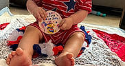 Eugene is registered to the contest to win money with this photo: baby, toddler, child, sitting, red_clothing, striped_shirt, star_design, blanket, indoor, living_room, carpet, curly_hair, cute, holding_object, celebration, foot, face, expression, toy, decor