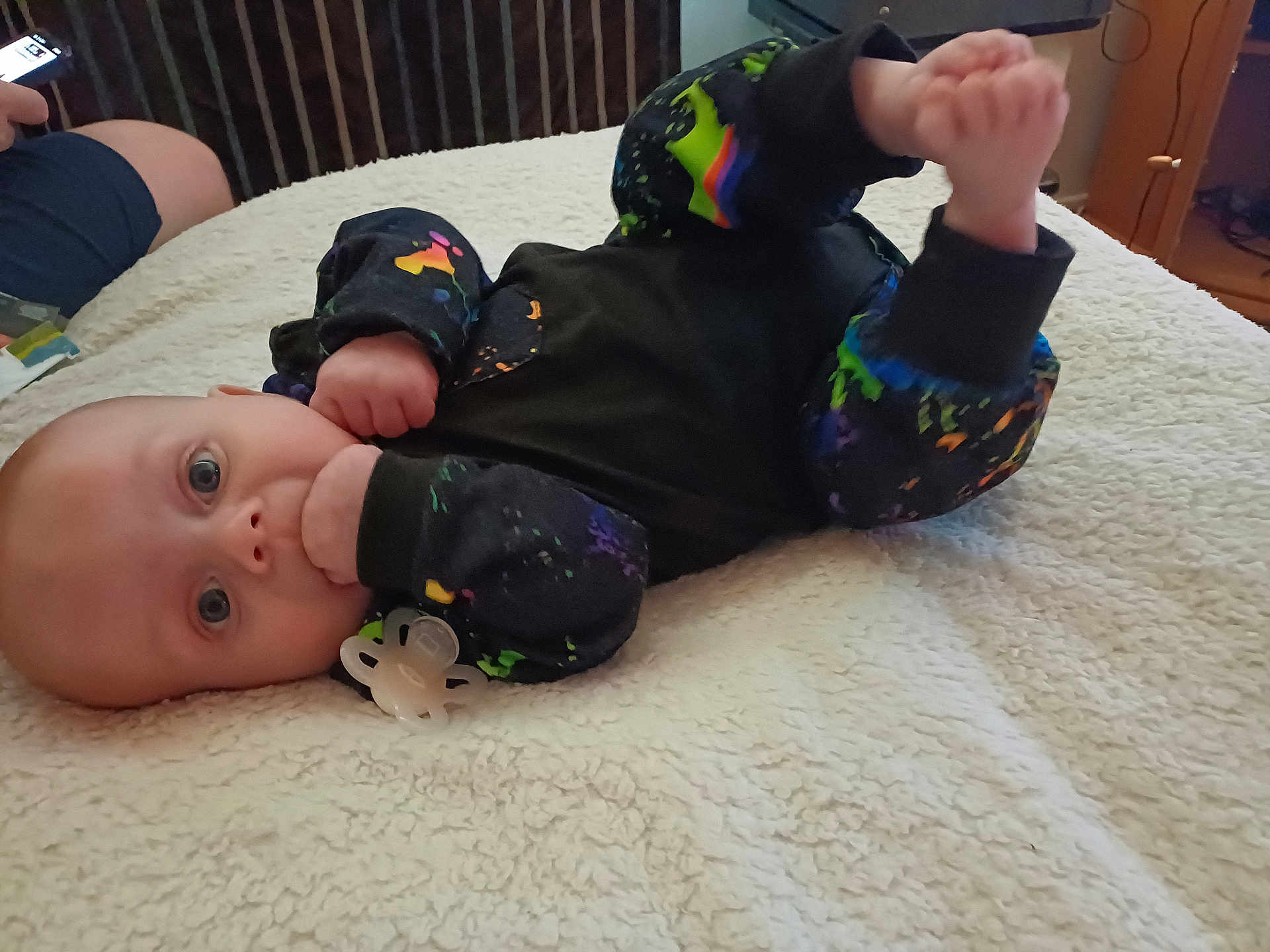 Jaydan is registered to the contest to win money with this photo: baby, infant, blanket, pacifier, hand, foot, clothing, colorful, lying_down, indoor, fist, face, blue_eyes, soft_texture, person, bed, adult_hand, phone, casual, cute