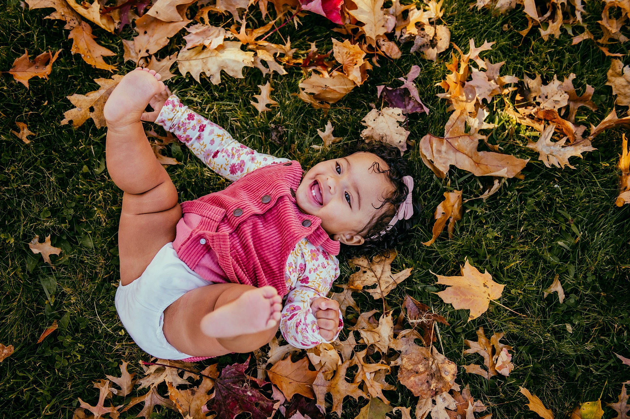 Maelynn is registered to the contest to win money with this photo: baby_toddler_clothing, botany, branch, deciduous, facial_expression, finger, fun, grass, happy, human_leg, joy, leaf, people, people_in_nature, person, petal, plant, playing_with_kids, smile, thigh