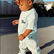 Eden participe au concours pour gagner de l'argent avec cette photo : toddler, child, curly_hair, white_clothing, sneakers, outdoor, street, sunlight, shadow, side_view, casual_wear, young_child, daytime, pavement, urban, portrait, fashion, cute, person, standing