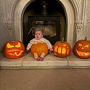 Autumn is registered to the contest to win money with this photo: baby, pumpkin, jack_o_lantern, halloween, carved_pumpkin, fireplace, candlelight, orange, costume, festive, holiday, child, cute, sitting, indoor, stone, carving, decor, celebration, feet
