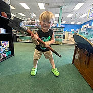 Wrangler joined the competition — help win amazing prizes! black_shirt, blond_hair, casual_clothing, ceiling_lights, child, collectibles, floor, green_carpet, happy, indoor, neon_shoes, person, playful, retail, shelves, shorts, smiling, standing, store, toy_hammer