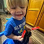 blond_hair, blue_shirt, cartoon_characters, chair, child, cute, food, happy, indoor, kitchen, person, playful, popsicle, shorts, smile, snack, summer, toddler, wooden_cabinet, wooden_floor