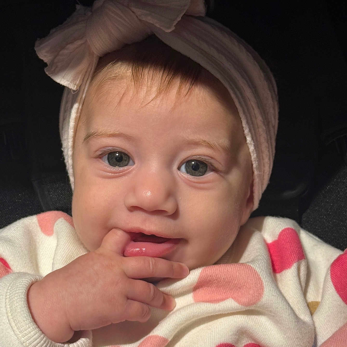 Livia is registered to the contest to win money with this photo: baby, infant, child, portrait, close_up, face, headband, bow, wide_eyed, smiling, hand, finger, mouth, eyes, pink, hearts, clothing, indoor, seated, photography
