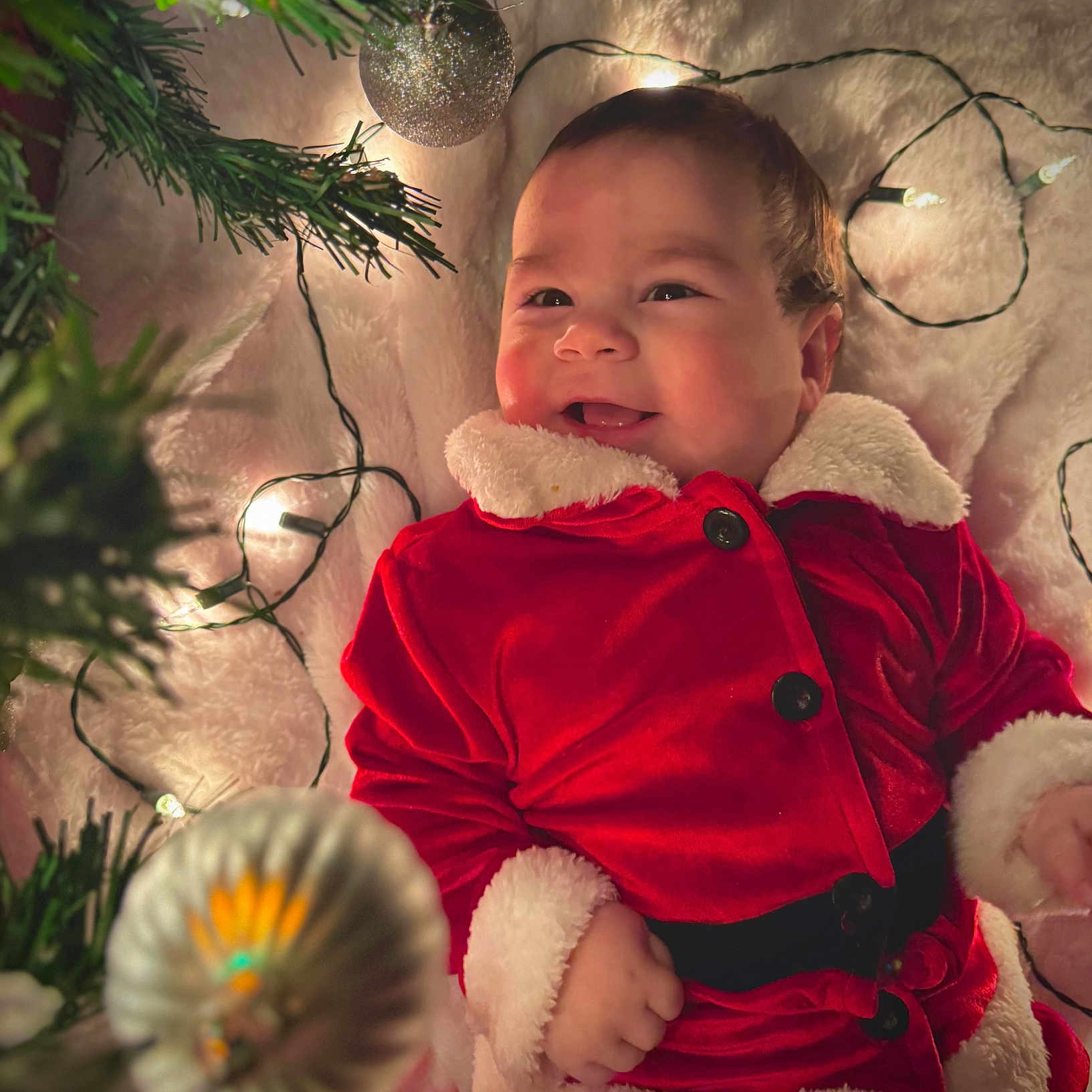 Noah Molina is registered to the contest to win money with this photo: baby, blanket, candid, celebration, child, christmas, cute, decoration, face, festive, happy, holiday, indoors, infant, lights, ornament, red_clothing, santa_suit, smiling, winter