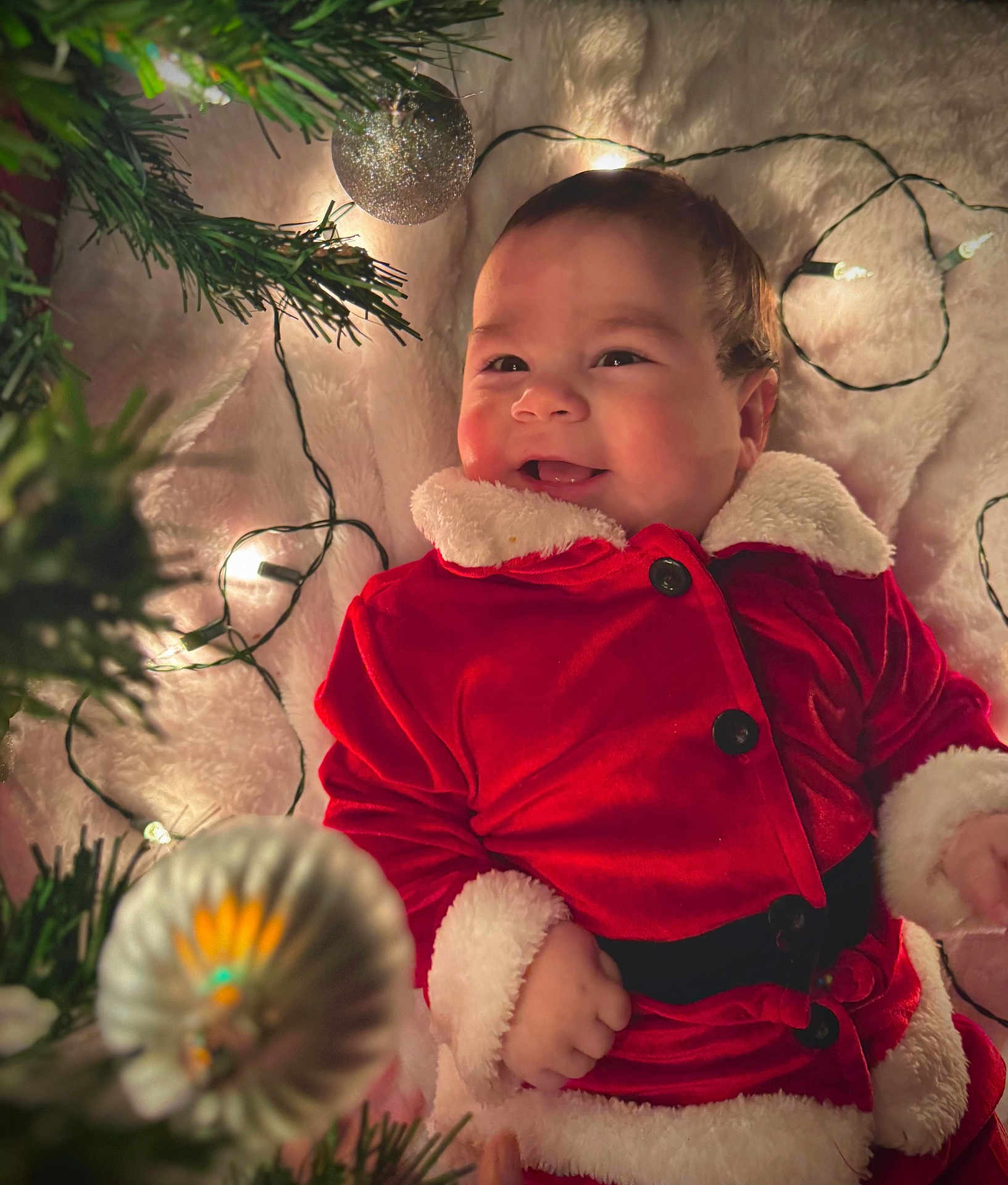 Noah Molina is registered to the contest to win money with this photo: baby, child, smiling, christmas, holiday, festive, red_clothing, santa_suit, blanket, lights, ornament, decoration, happy, face, infant, candid, cute, celebration, winter, indoors