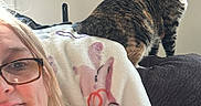 Snickers joined the competition — help win amazing prizes! woman, glasses, cat, tabby_cat, indoor, couch, blanket, clock, wall, relaxed, home, furniture, portrait, seated, light_switch, casual, pet, companion, comfort, smile