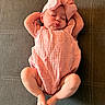 baby, infant, pink_bow, pink_outfit, lying_down, arms_up, puckered_lips, sleeping, cute, child, soft_fabric, texture, brown_background, adorable, peaceful, resting, small_feet, headband, closeup, human