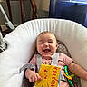 baby, smiling, infant, toy, book, baby_chair, cushion, indoors, child, happy, seat, colorful, fabric, pink_clothing, play, cute, person, young_child, home, window
