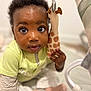 baby, child, toy, giraffe, curly_hair, big_eyes, cute, infant, play_area, soft_toy, clothing, sitting, indoor, portrait, close_up, skin, hand, pink_socks, striped_sleeves, yellow_shirt