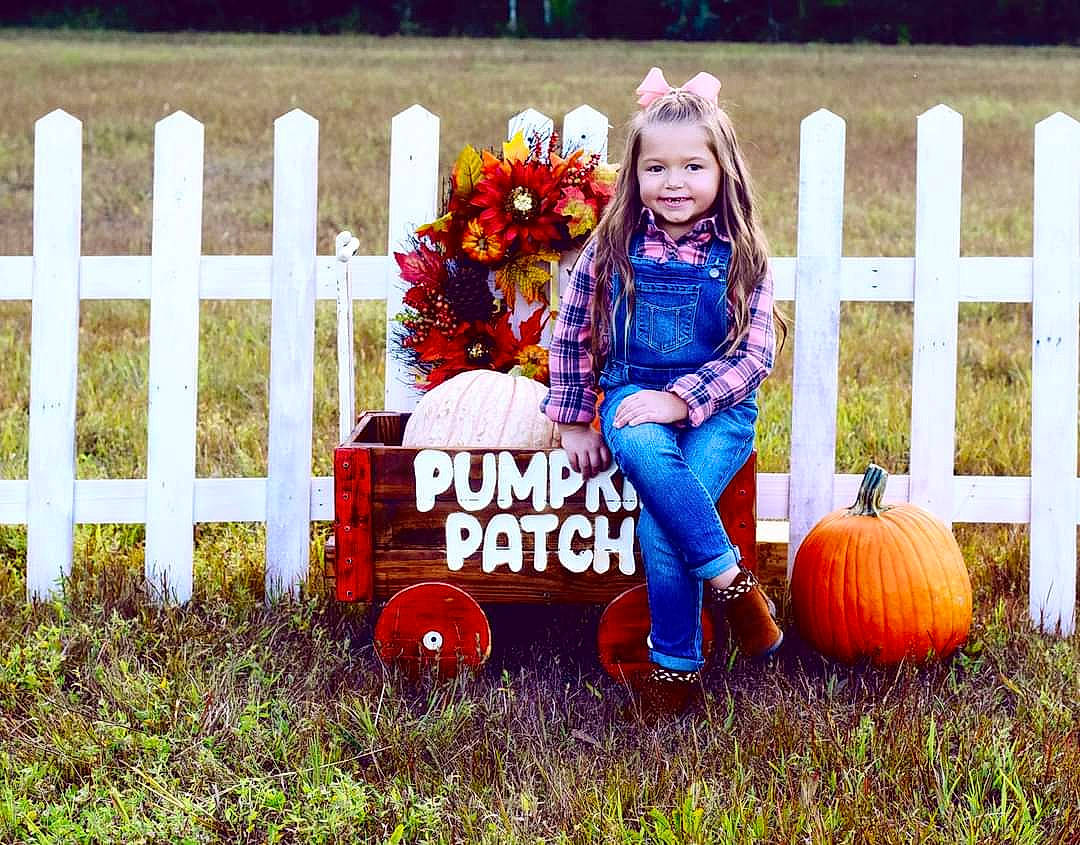 Justice is registered to the contest to win money with this photo: calabaza, cucurbita, dress, eye, fence, flower, footwear, gourd, grass, happy, joy, mammal, orange, people_in_nature, person, plant, pumpkin, shoe, tire, toddler