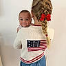 child, baby, braid, red_bow, sweater, american_flag, shorts, smile, holding, indoor, person, hair, cute, portrait, face, happy, child_holding_baby, back_view, casual_clothing, young