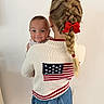 Cash is registered to the contest to win money with this photo: baby, child, girl, braid, red_bow, smiling, sweater, american_flag, indoor, white_wall, shorts, holding, portrait, cute, happy, person, face, hair, fashion, casual