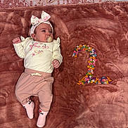 Lia Vana joined the competition — help win amazing prizes! baby, girl, pacifier, headband, blanket, pink_clothing, white_top, beads, number_two, floor_tiles, indoor, cute, child, infant, lying_down, soft_texture, colorful, decor, small_person, socks