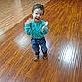 brown_shoes, casual_clothing, child, curious, cute, flooring, indoor, jeans, motion_blur, person, real_photo, small_toy, smiling, standing, sweatshirt, toddler, toy, waving_hand, wooden_floor, young_child