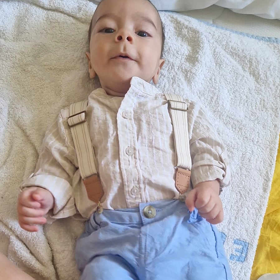 Mael participe au concours pour gagner de l'argent avec cette photo : baby, bed, child, clothing, cute, fabric, face, foot, hand, indoors, infant, looking, lying_down, person, shirt, shorts, smile, soft, suspenders, towel