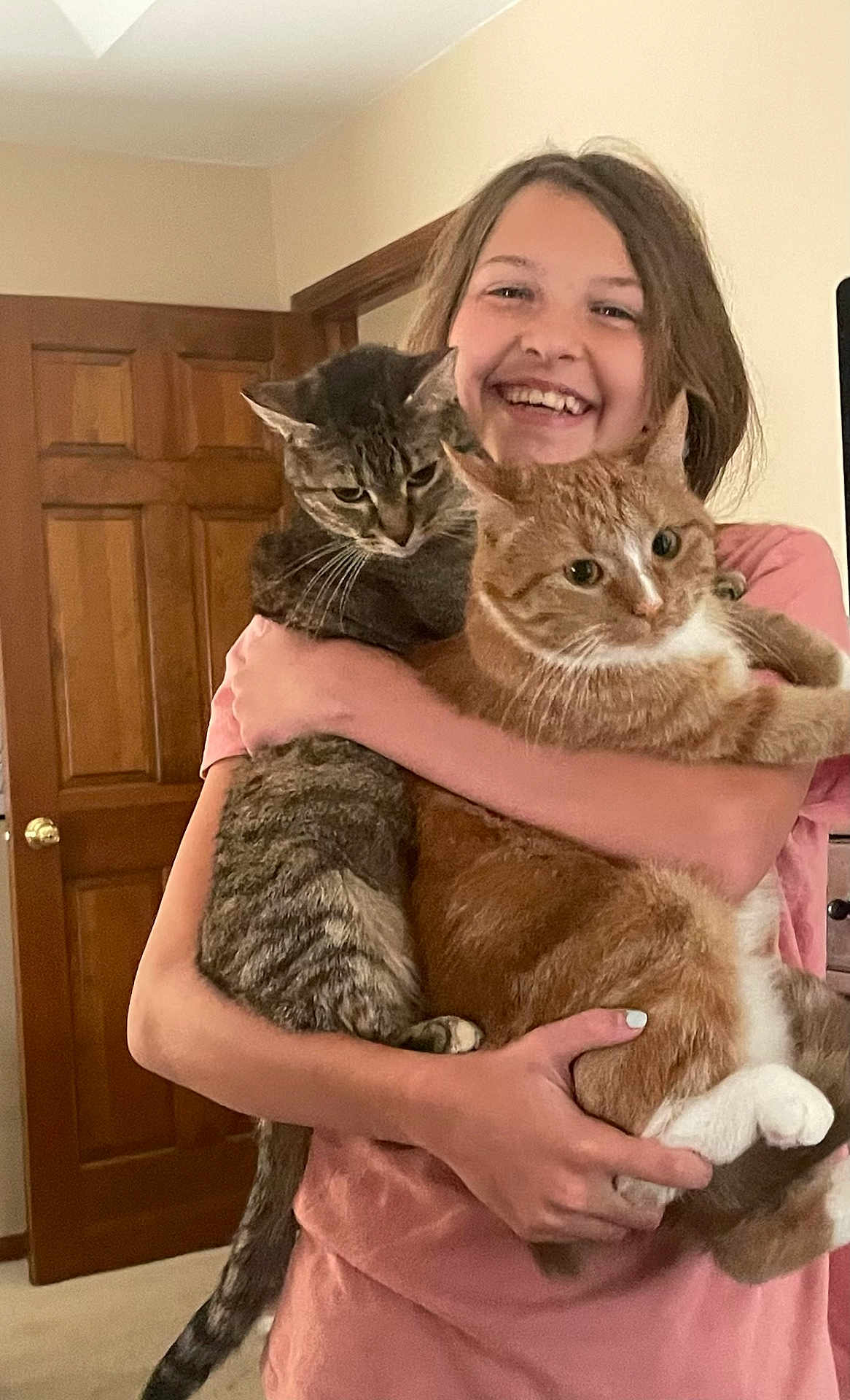 Nancy Rhoades joined the competition — help win amazing prizes! animal, carpet, cat, cute, domestic, feline, happy, holding, home, hugging, indoor, orange_cat, person, pet, pink_shirt, short_sleeves, smiling, tabby_cat, wooden_door, young_person