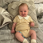 Thomas is registered to the contest to win money with this photo: baby, infant, smiling, knitwear, pillow, bed, pacifier, beaded_pacifier_clip, sock, cute, child, indoor, comfort, happy, person, portrait, sitting, soft_fabric, relaxation, cozy