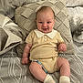baby, infant, smiling, knitwear, pillow, bed, pacifier, beaded_pacifier_clip, sock, cute, child, indoor, comfort, happy, person, portrait, sitting, soft_fabric, relaxation, cozy