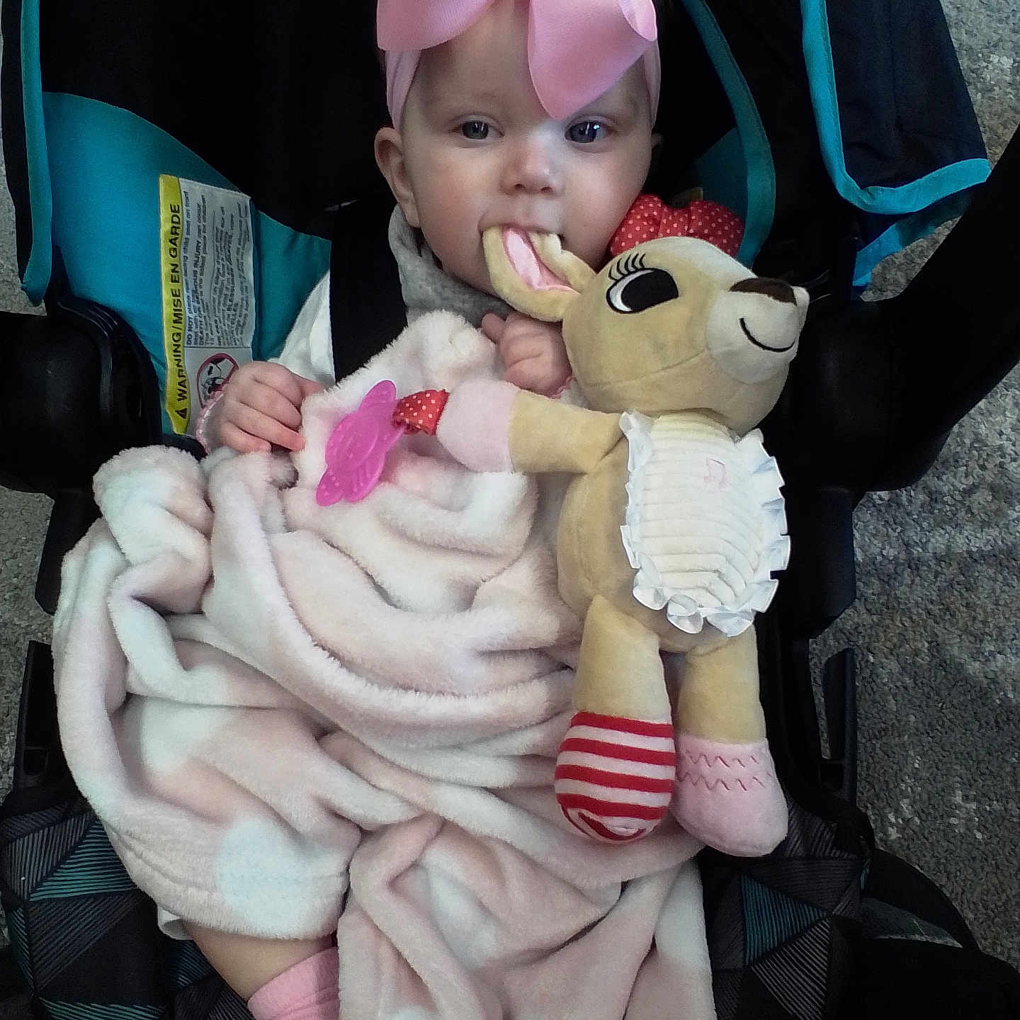 Journey is registered to the contest to win money with this photo: baby, blanket, car_seat, car_seat_strap, carpet, chewing, child, comfort, cute, face, headwear, indoor, infant, person, pink_bow, pink_socks, plush_toy, seated, soft_toy, toy