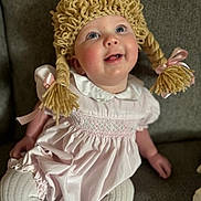 Journey is registered to the contest to win money with this photo: baby, child, knitted_hat, braids, pink_dress, white_tights, couch, smiling, happy, indoor, portrait, cute, childhood, young, sitting, person, face, headwear, apparel, cozy