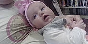 Journey is registered to the contest to win money with this photo: baby, child, person, headband, pink, bow, clothing, hand, sleeve, bookshelf, books, library, indoor, couch, arm, face, eyes, portrait, resting, comfort
