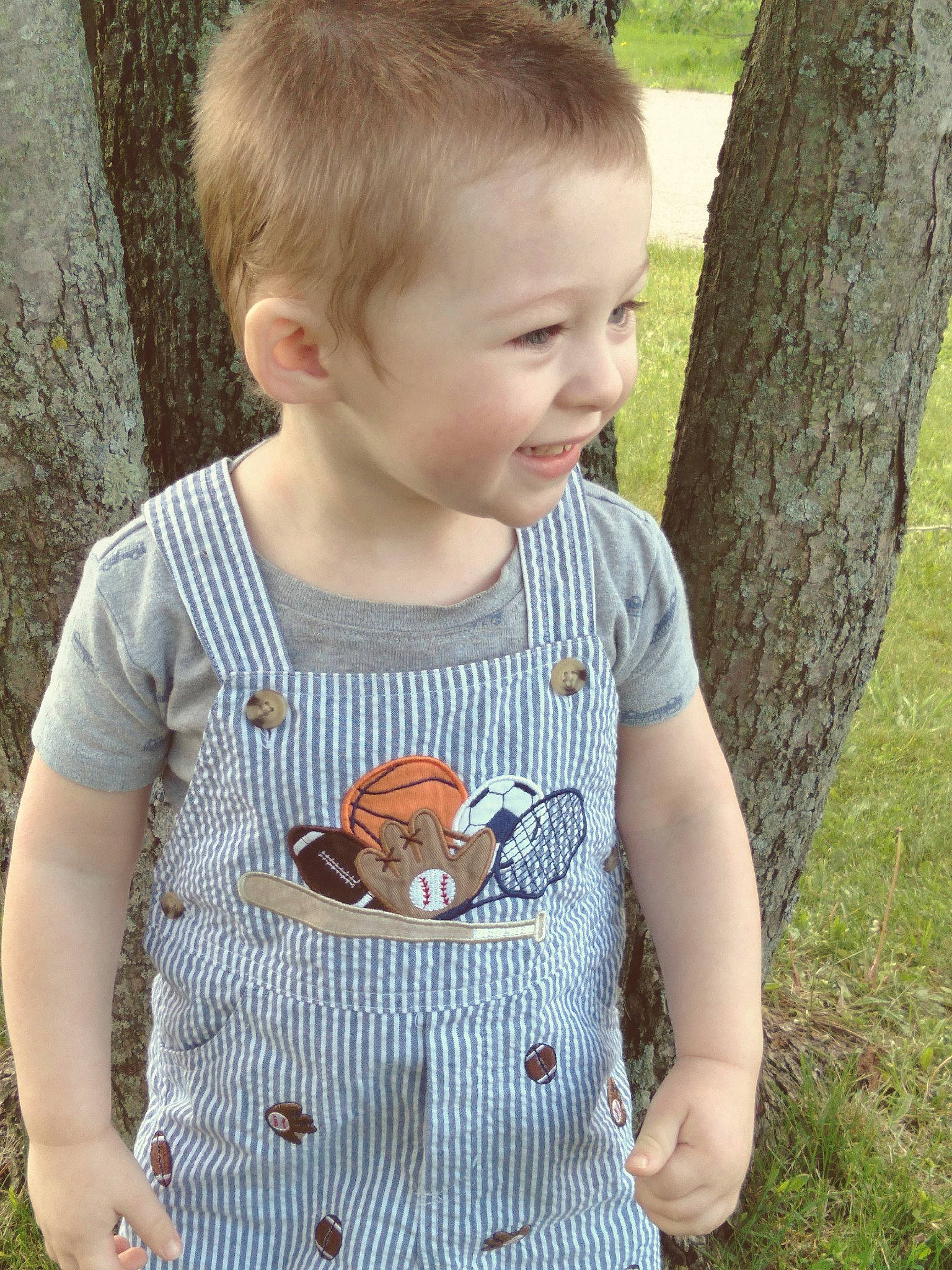 Mavrick is registered to the contest to win money with this photo: baby_toddler_clothing, cool, facial_expression, gesture, grass, grey, happy, joy, leaf, mammal, neck, nose, person, photograph, plant, sleeve, smile, standing, t_shirt, toddler