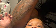 Austin is registered to the contest to win money with this photo: baby, infant, tattoo, arm, person, skin, face, clothing, blue, hand, indoor, bottle, container, black_shirt, curious, closeup, expression, casual, relaxed, home