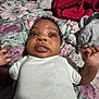 Austin joined the competition — help win amazing prizes! baby, infant, white_onesie, bedspread, floral_pattern, toy, plush_elephant, red_cloth, curious_expression, wide_eyes, hand, lying_down, indoor, child, person, face, cute, soft_lighting, close_up, bedroom
