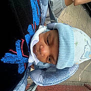Austin joined the competition — help win amazing prizes! baby, infant, blue_hat, baby_carrier, blanket, person, outdoor, sidewalk, arm, brick_wall, clothing, face, headwear, curious, close_up, street, urban, daylight, casual, child