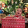 Lucas is registered to the contest to win money with this photo: baby, child, christmas_tree, gift_box, presents, holiday, festive, red_clothing, smiling, indoors, decorations, celebration, happy, face, pattern, wooden_floor, christmas_decor, cheerful, festivity, joy