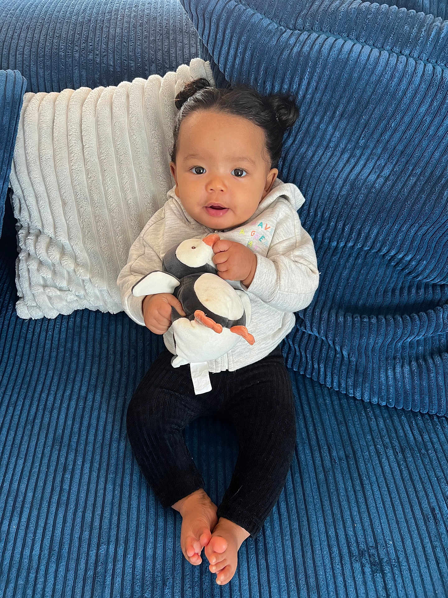 Madison a rejoint le concours — aidez-le/la à gagner de superbes lots ! baby, child, plush_toy, penguin, couch, blue_couch, pillow, white_pillow, black_pants, hoodie, indoor, barefoot, cute, smiling, portrait, seated, cozy, hair_buns, infant, happy
