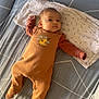 baby, infant, couch, pillow, onesie, orange_clothing, lion_print, blanket, indoor, child, lying_down, face, head, person, soft_lighting, patterned_fabric, comfortable, resting, small_child, cute