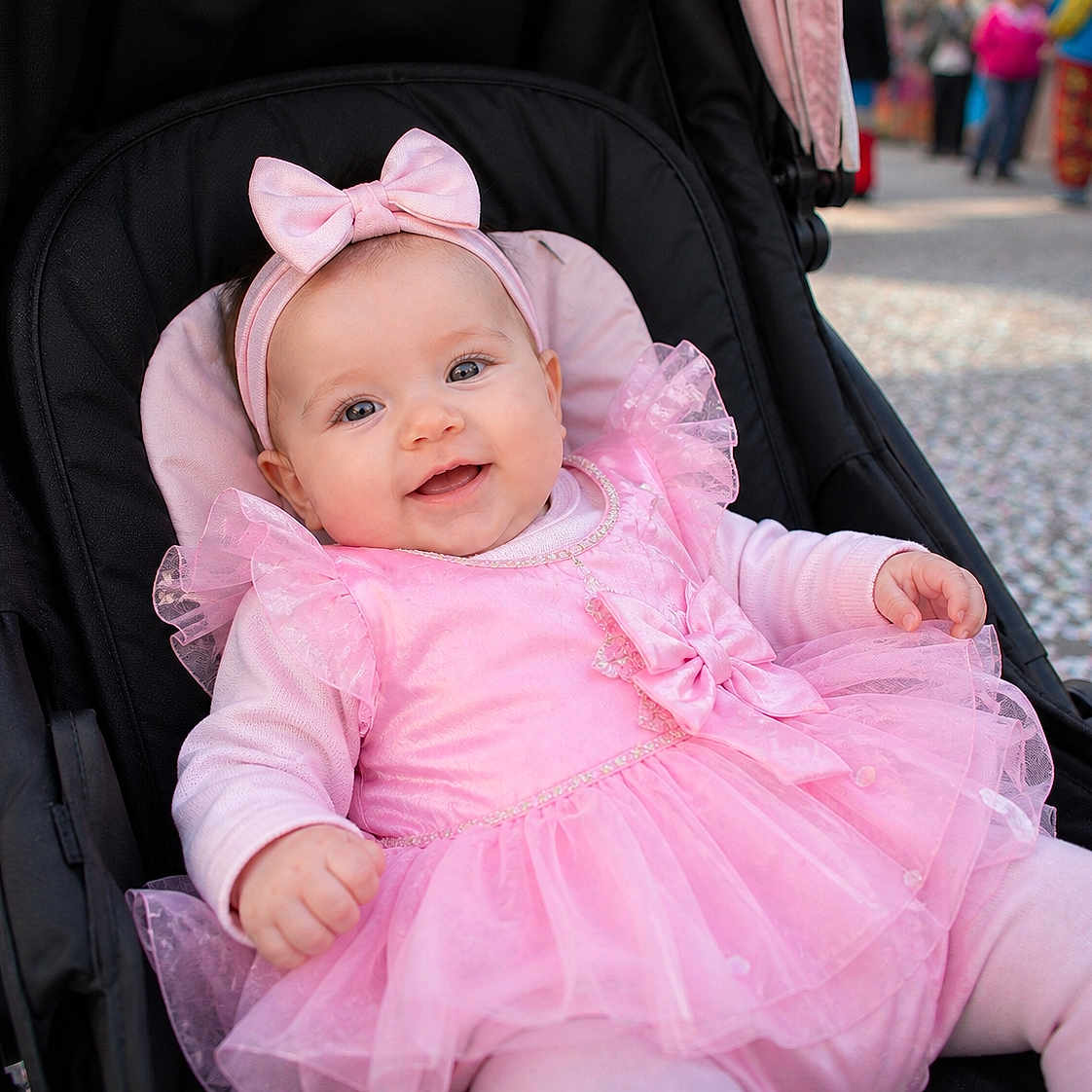 Arine participe au concours pour gagner de l'argent avec cette photo : baby, child, pink_dress, headband, stroller, smiling, outdoor, happy, portrait, cute, infant, tulle, clothing, person, face, seat, people, daylight, fashion, accessory