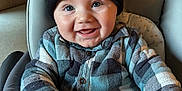 Lyam participe au concours pour gagner de l'argent avec cette photo : baby, child, infant, hat, pom_poms, plaid_shirt, high_chair, smiling, happy, indoors, drool, face, hands, blue, black, clothing, person, cute, portrait, seated