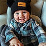 baby, child, infant, hat, pom_poms, plaid_shirt, high_chair, smiling, happy, indoors, drool, face, hands, blue, black, clothing, person, cute, portrait, seated