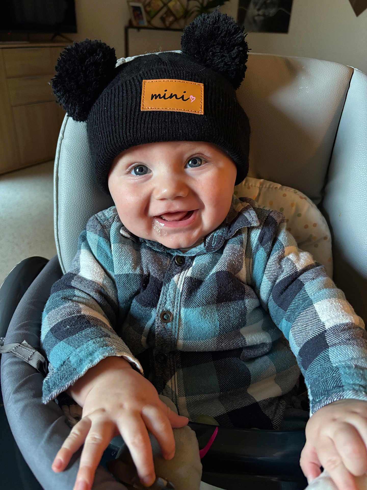 Lyam participe au concours pour gagner de l'argent avec cette photo : baby, child, infant, hat, pom_poms, plaid_shirt, high_chair, smiling, happy, indoors, drool, face, hands, blue, black, clothing, person, cute, portrait, seated