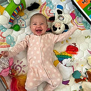 Rora joined the competition — help win amazing prizes! baby, infant, smile, pink_onesie, toys, plush_toy, pop_it, dinosaur_toy, keyboard_toy, playmat, colorful, happy, child, lying_down, indoor, cute, panda_plush, doll, playtime, soft